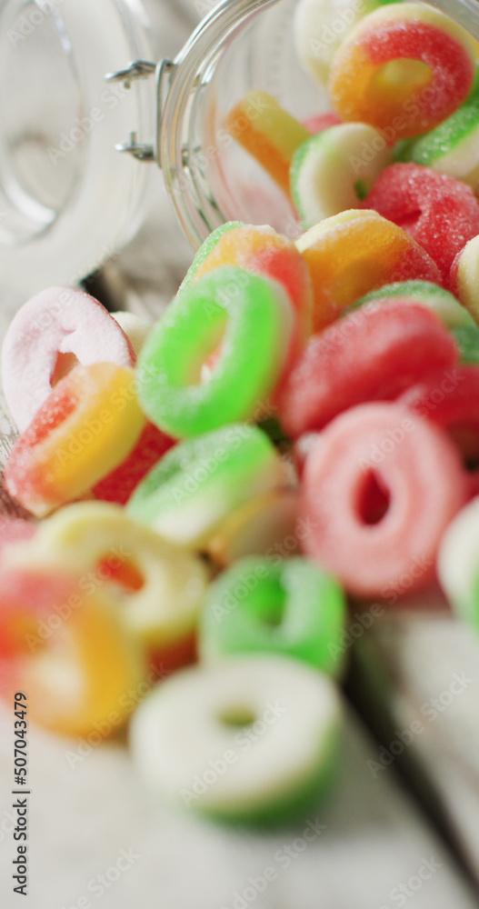 Vertical image of jelly candy spilling out of glass jar on wooden background