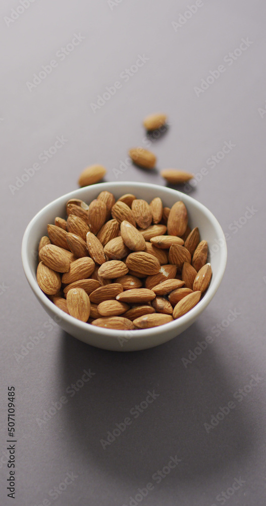 Vertical image of a bowl of almonds on a lilac background