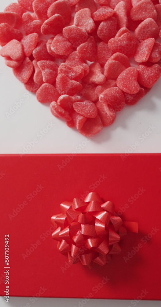 Vertical image of overhead view of red candies in heart shape, and wrapped gift on white