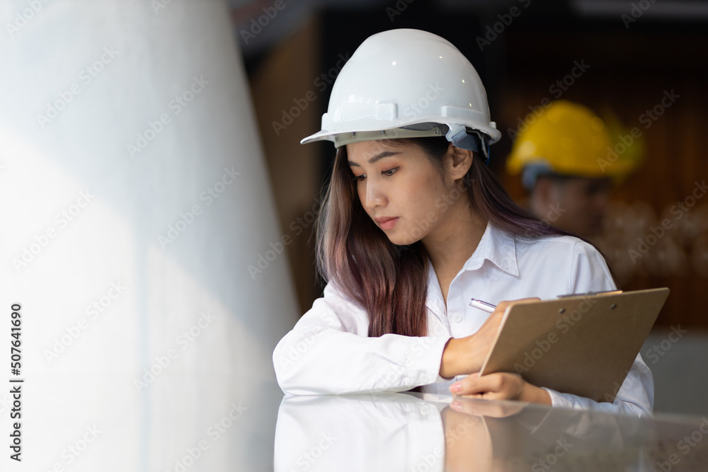 Young architect or engineer working in an office is writing a note on the design of a building model