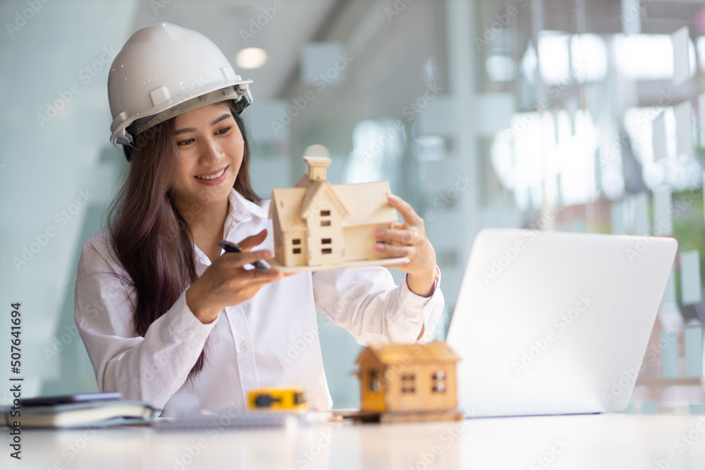 Female architect designer in an office working on a laptop is modeling a house and writing a housing