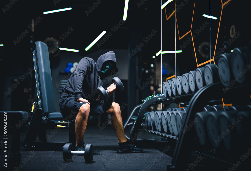 Strong fit healthy man in dark hoodie. Mystery man posing with hoodie on a black background.