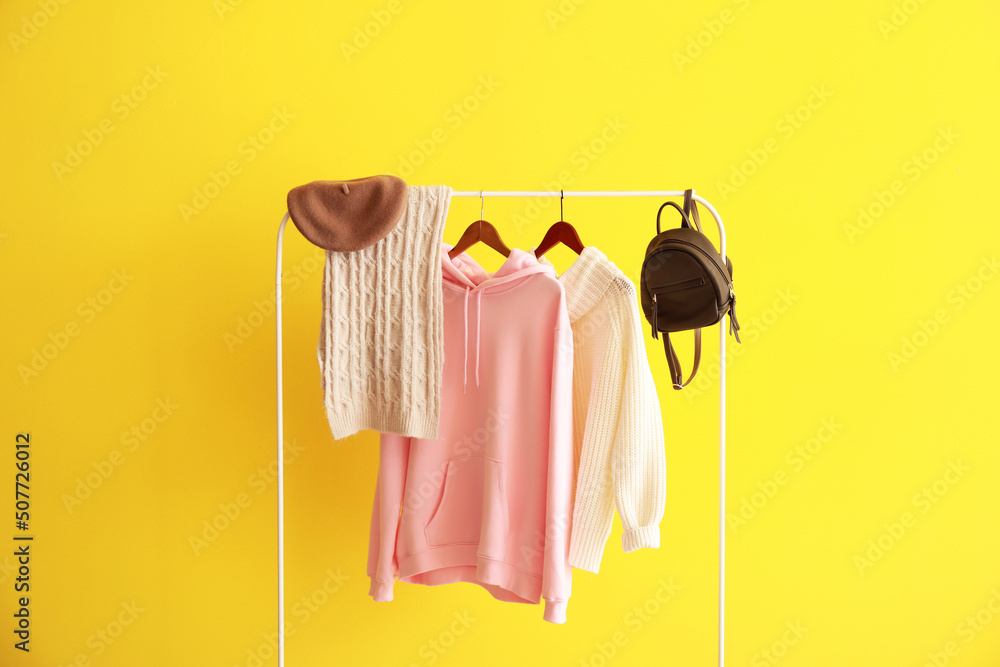 Rack with warm female clothes and accessories near yellow wall