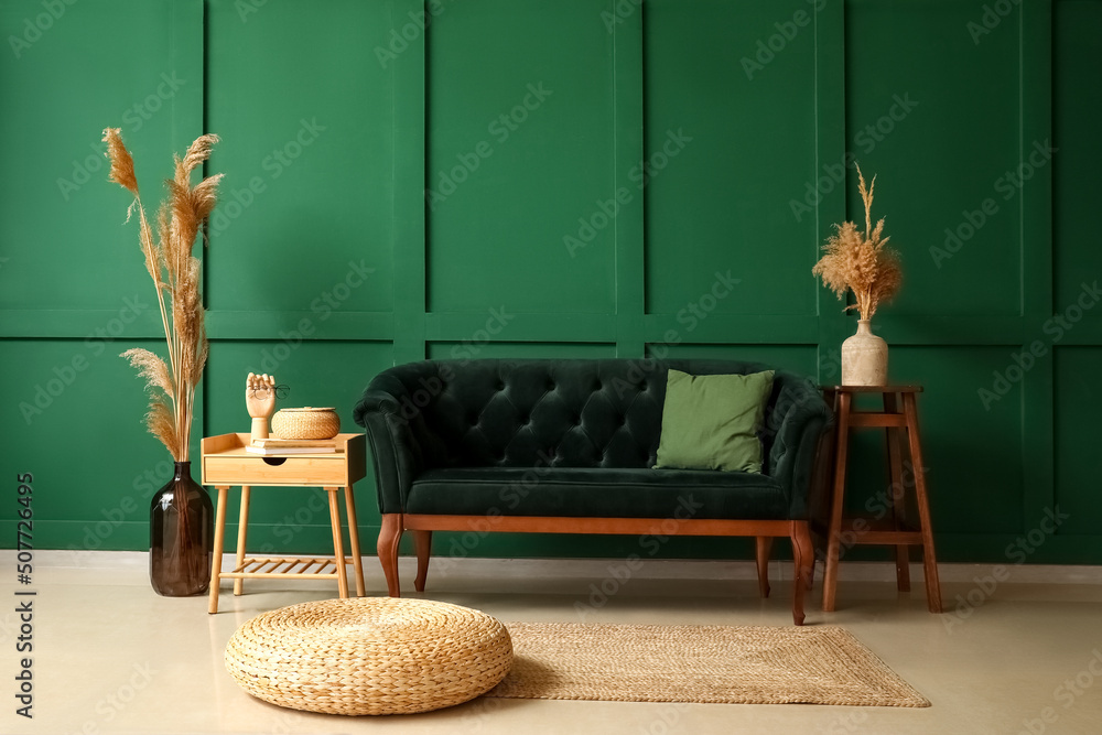 Stylish sofa, pouf and table near green wall