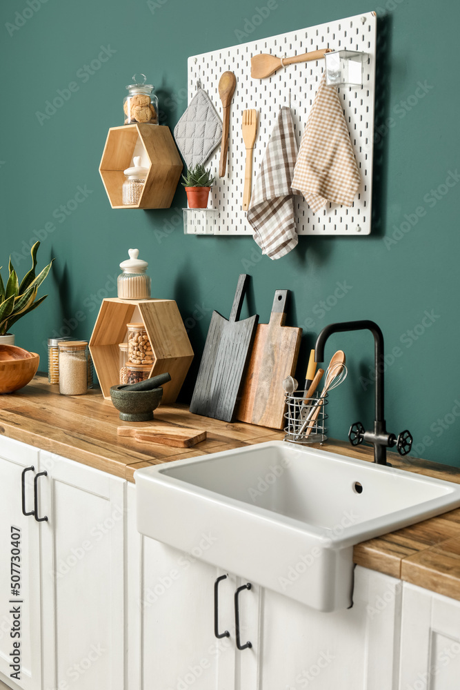 Cutting boards with kitchen utensils and sink on counters near green wall