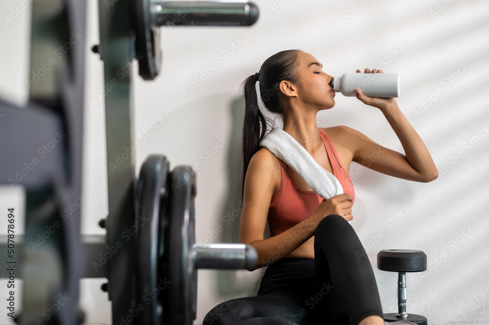 Woman sport girl sitting resting after work out drinking water at fitness with fore ground of exerci