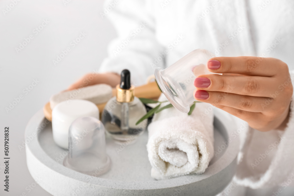 Woman holding tray with bath supplies and vacuum jars for anti-cellulite massage on light background