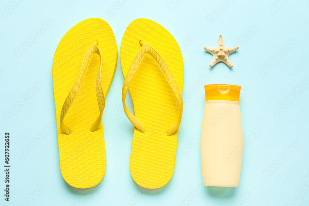 Bottle of sunscreen with flip flops and starfish on blue background