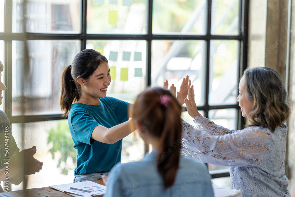 Diverse group of smiling young business people celebrating success with high fives while working tog