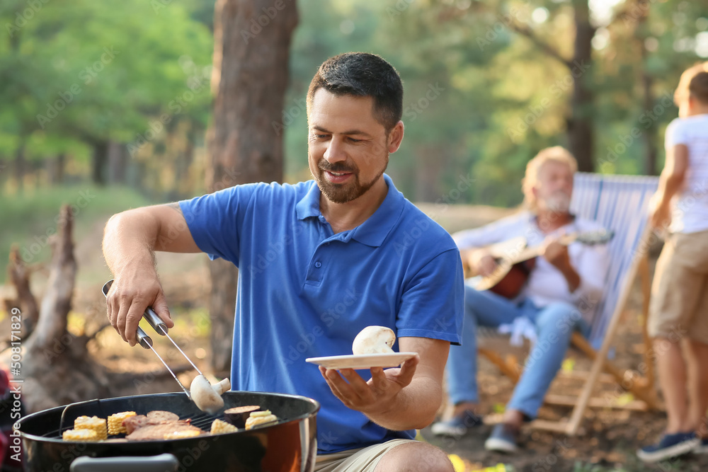 Handsome man cooking food on grill at barbecue party