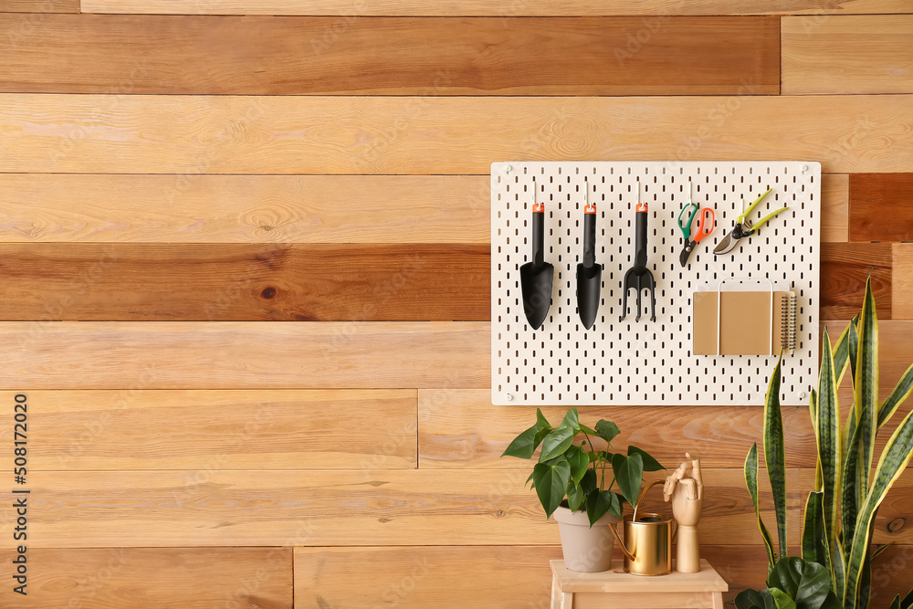 Pegboard with gardening tools and stepladder stool with houseplants on wooden wall