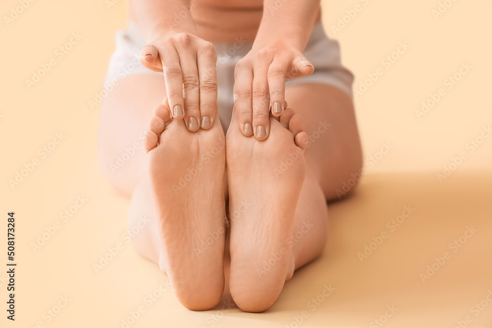 Young woman making foot massage on beige background, closeup