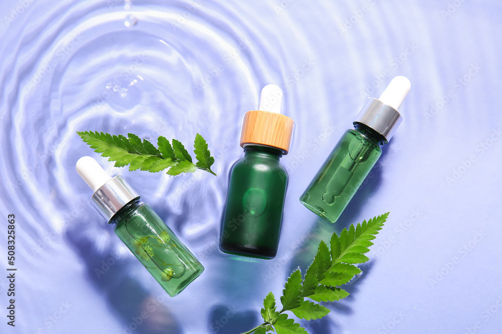 Bottles of natural serum and fern leaves in water on lilac background