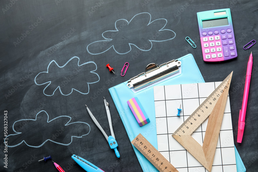 Stationery supplies and drawn clouds on school blackboard