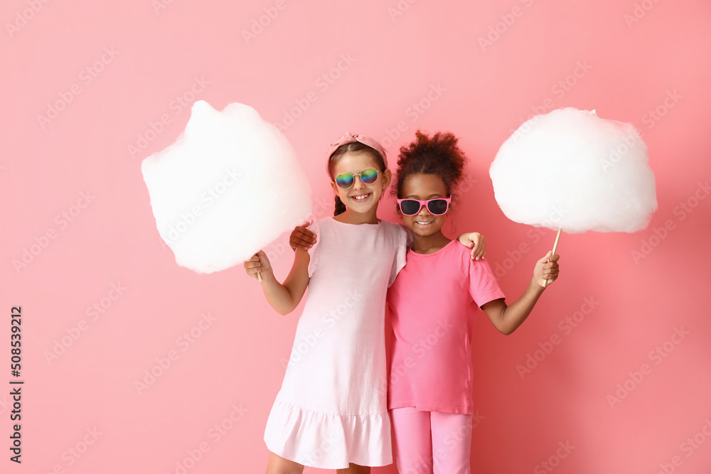 Cute little girls with cotton candy on pink background