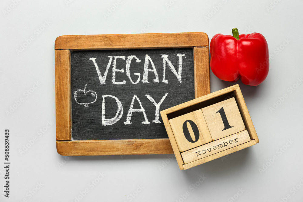 木制立方体日历，日期为11月1日，甜椒和木板，灰色背景上写着VEGAN DAY