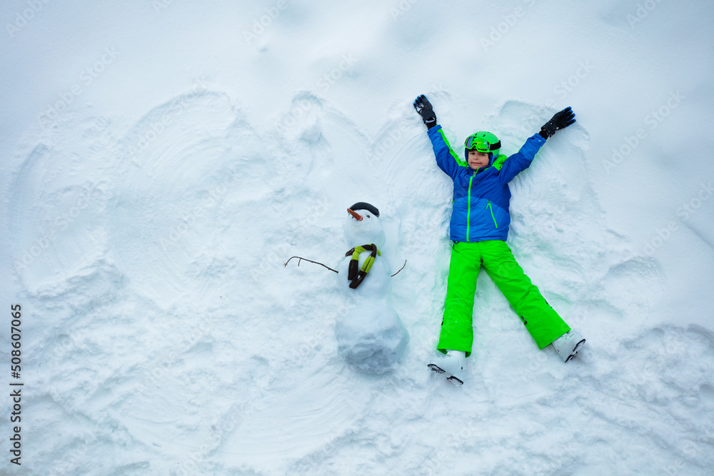 滑雪男孩躺在雪地里，戴着滑雪帽从上面看