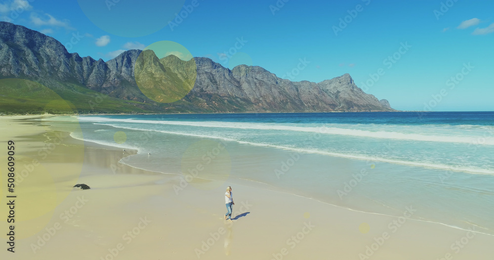 Multiple light spots floating against caucasian woman walking at the beach