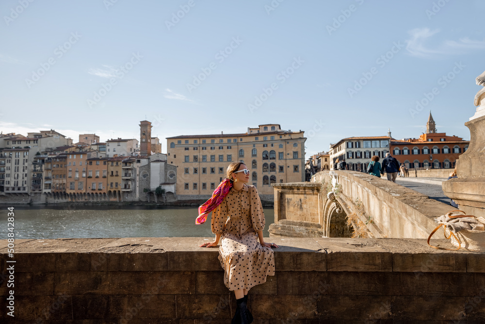 Young woman sitting on the riverside of Arno river, traveling old town in Florence. Happy traveler v