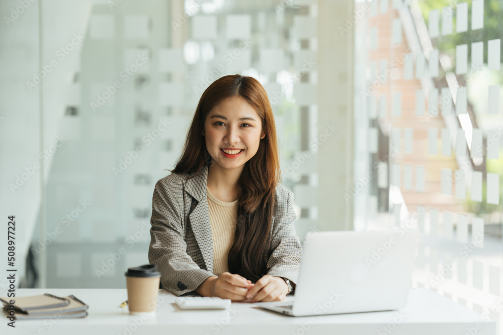 年轻漂亮的女人坐在工作场所的椅子上使用笔记本电脑，小企业