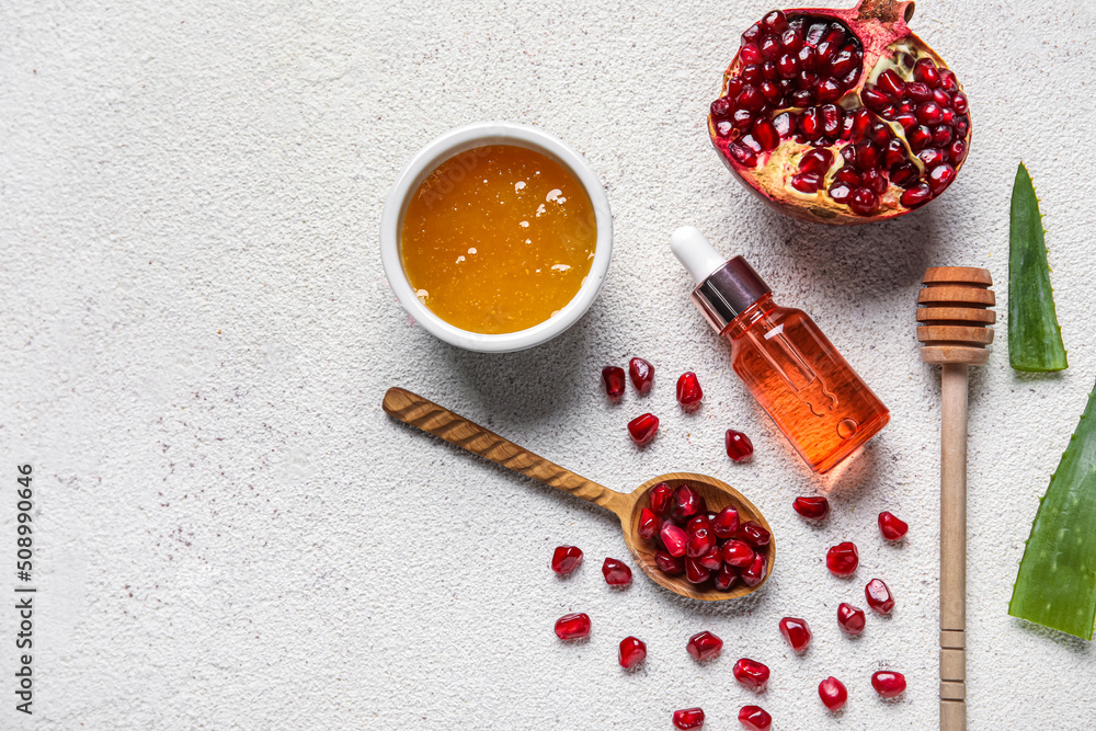 Bottle of natural serum, spoons with pomegranate, honey and aloe leaves on white background