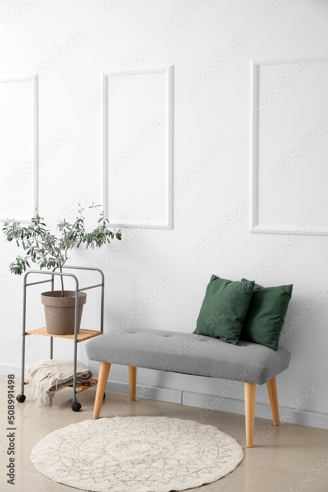 Soft bench with pillows and shelving unit near light wall