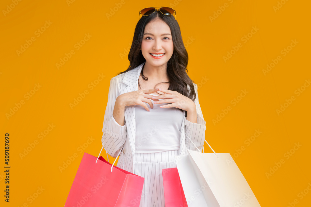 Asian happy female woman girl holds colourful shopping packages   standing on yellow background stud