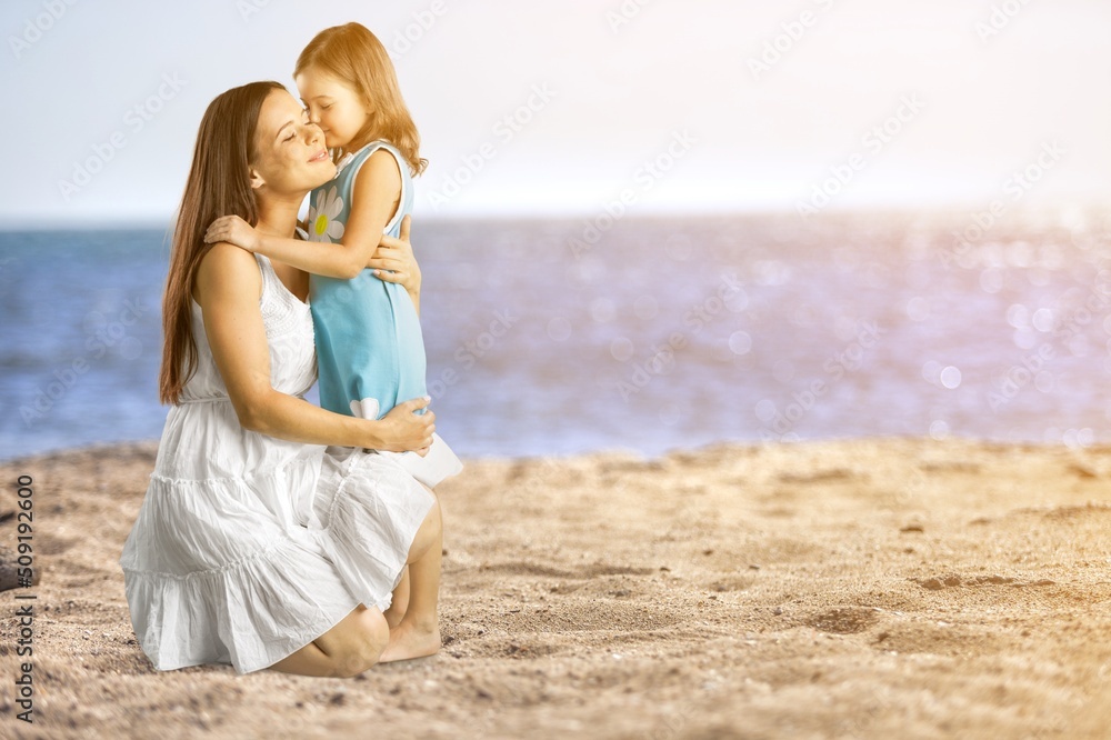 Young woman with her little cute girl on beach during sunset. Cheerful and cute daughter walking and