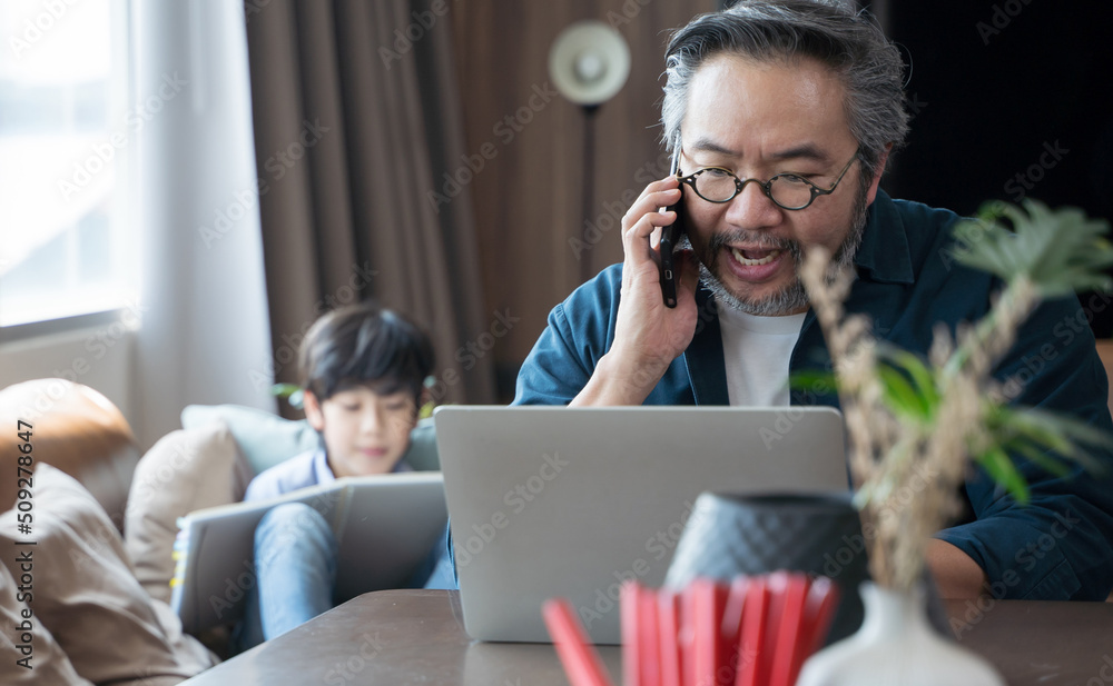 一名亚洲中年男子带着儿子在家用笔记本电脑工作，在背面画了一幅画。