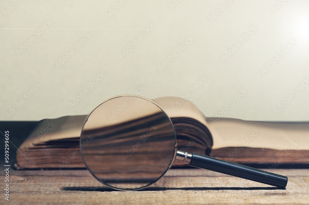 Magnifying glass and opened book on the desk, learning, research searching information concept