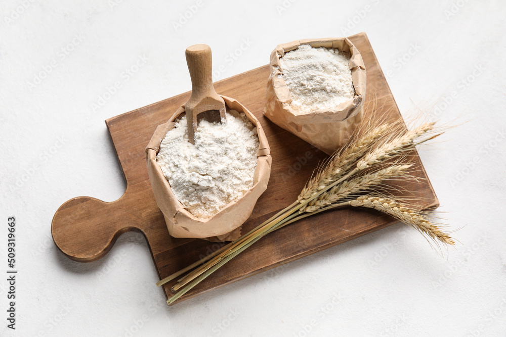 Bags with wheat flour on wooden board against white background