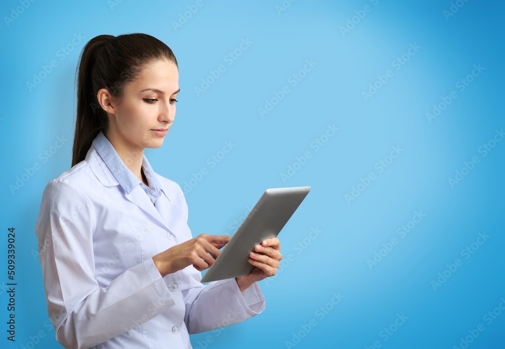 Beautiful young girl doctor, with digital table on a blue background. Medical student practitioner. 