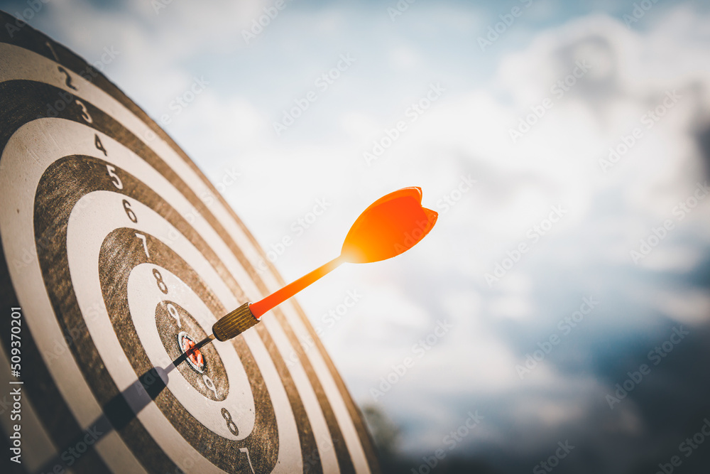 Close up shot red darts arrows in the target  of dartboard center on dark blue sky background. Busin