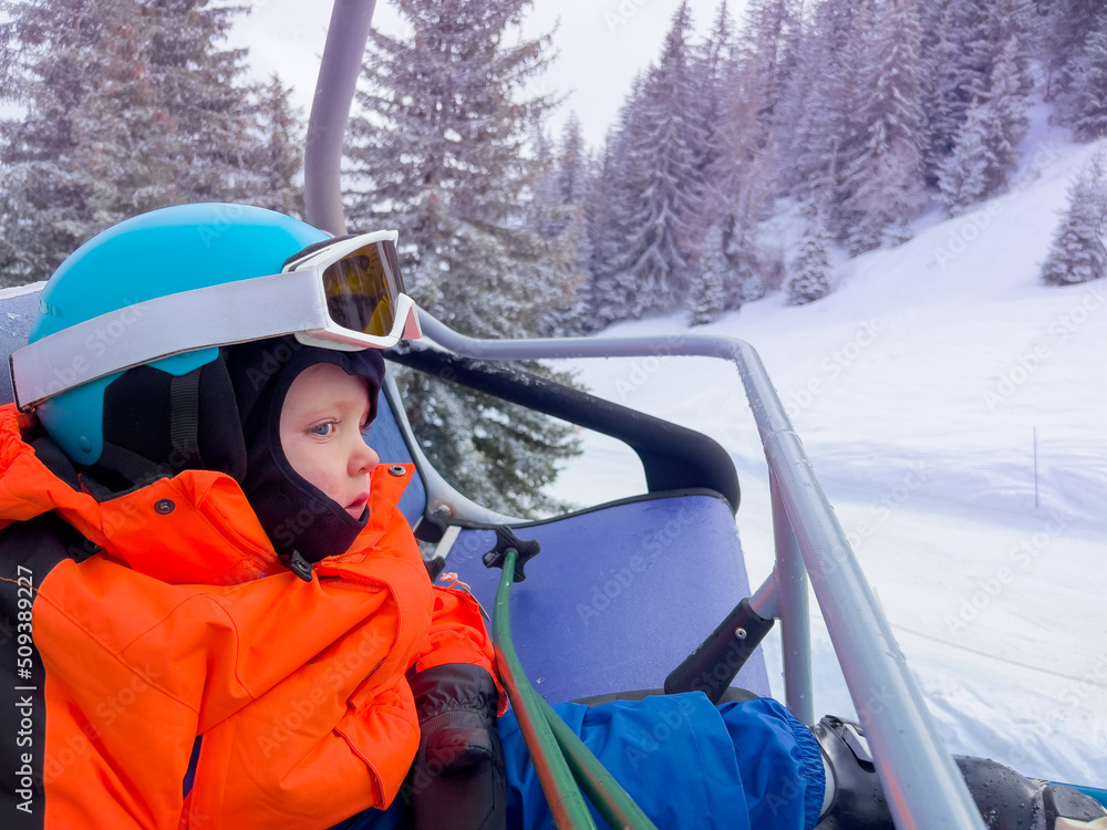 Little boy sit in ski chairlift on alpine sport resort