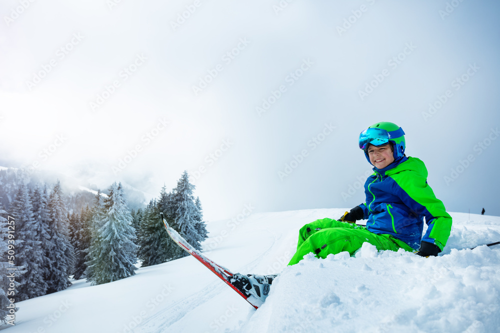 拥有高山天空的男孩坐在雪地里微笑，侧视