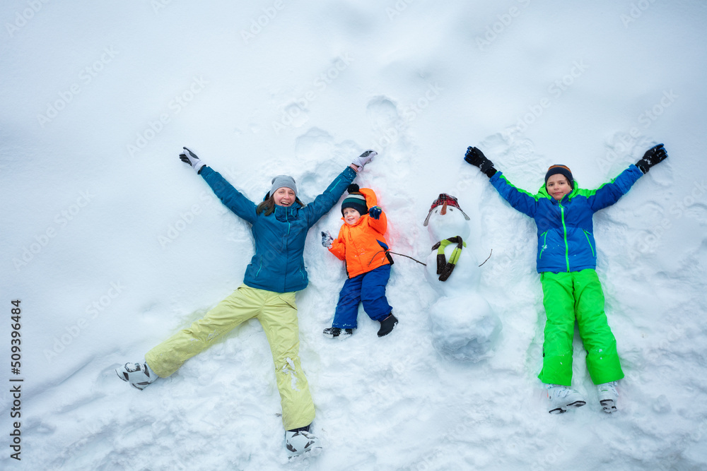 母亲和两个男孩与雪人躺在雪地里，俯视图