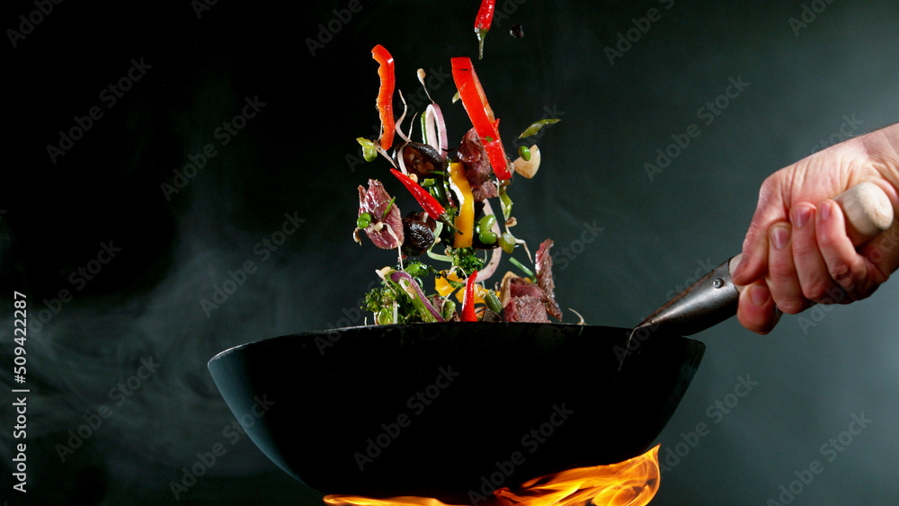 Closeup of chef throwing beef pieces with vegetable.