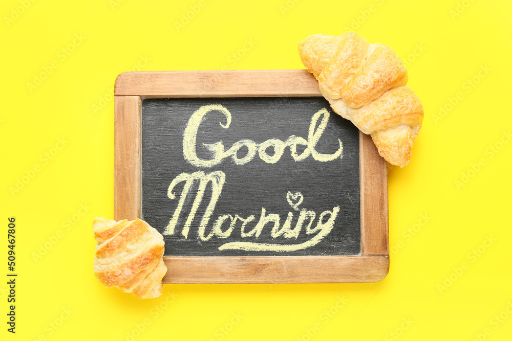 Chalkboard with text GOOD MORNING and tasty croissants on yellow background