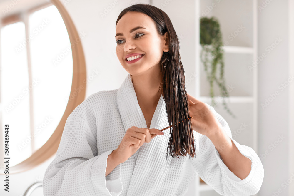 Young woman brushing her hair in bathroom