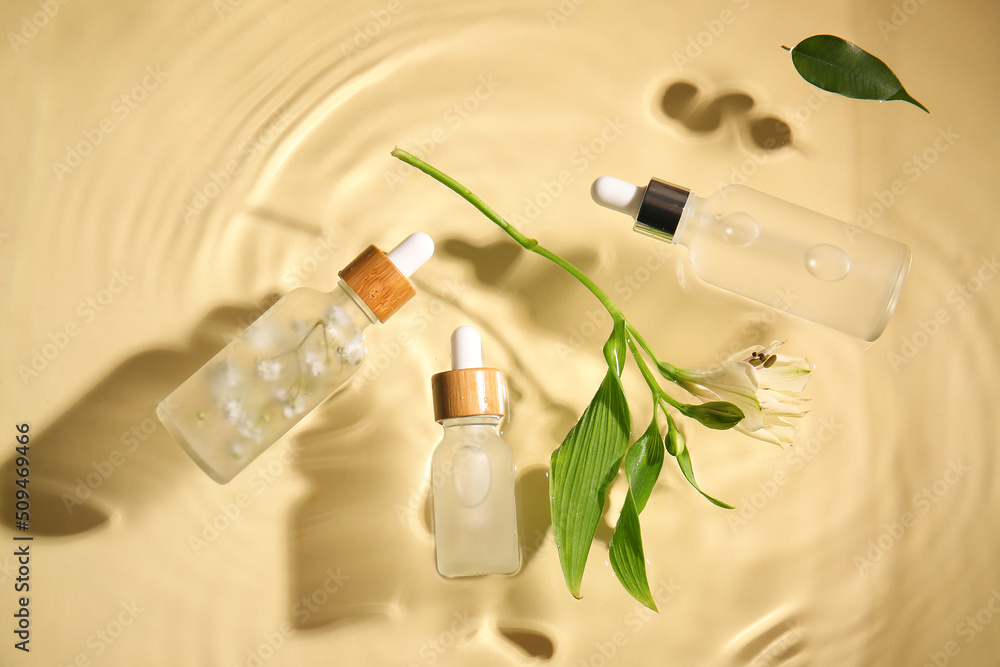 Bottles of natural serum and flower in water on color background