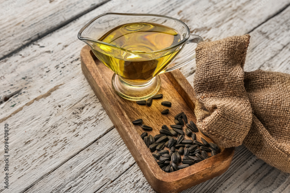 Gravy boat of oil, sunflower seeds, board and bag on white wooden background