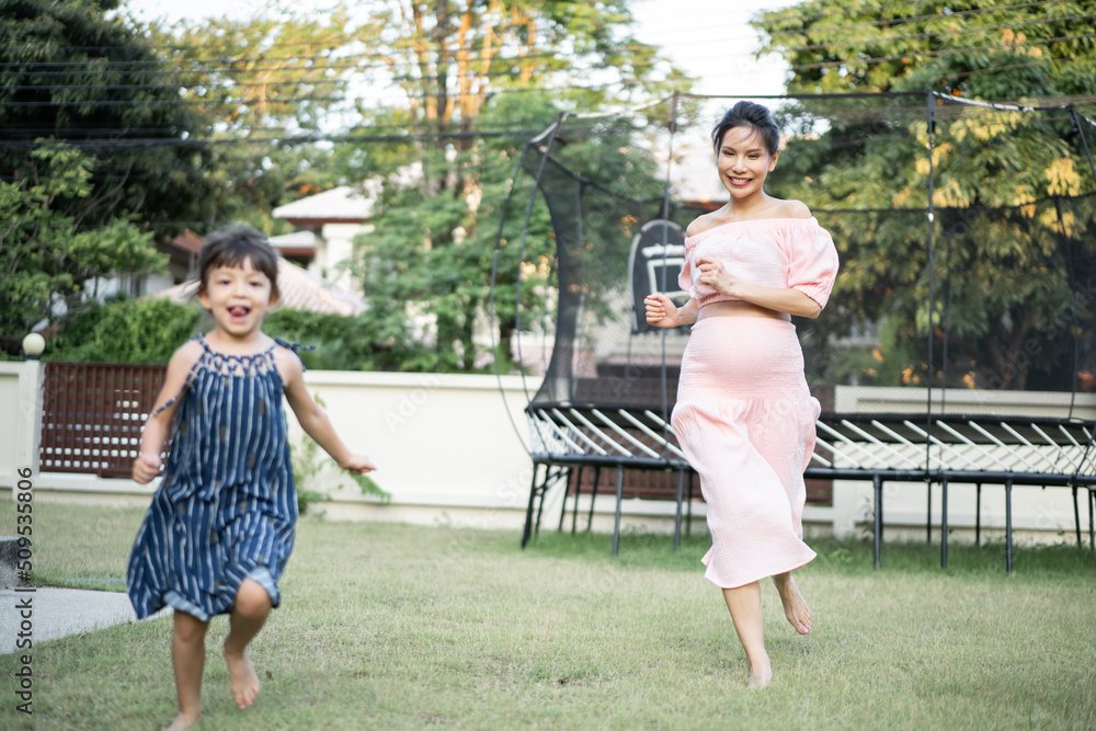 Asian pregnant mother playing with young daughter outdoor in backyard.