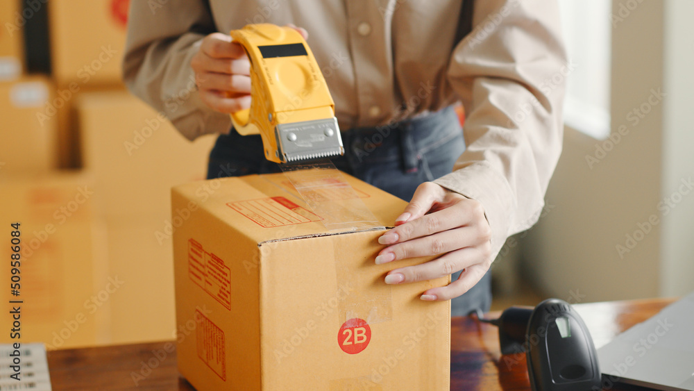 Asian woman working at online store warehouse packing product to parcel cardboard boxes, online e-co