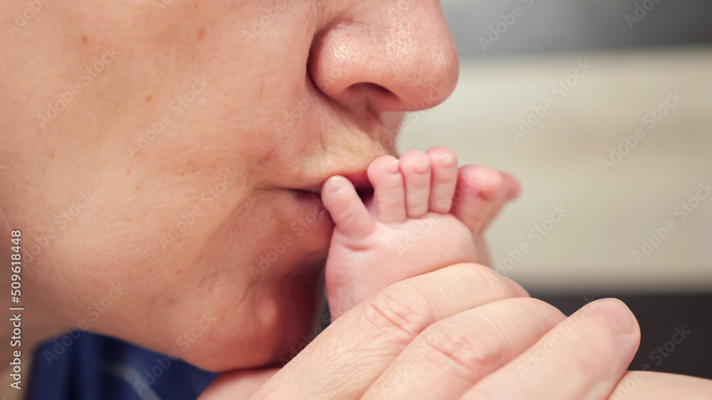 奶奶在模糊的背景下用新生婴儿的小手指亲吻裸露的小脚。女人在表演