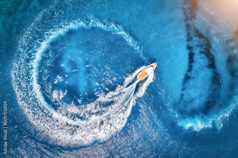 Aerial view of the speed boat in clear blue water at sunset in summer. Top view from drone of fast f