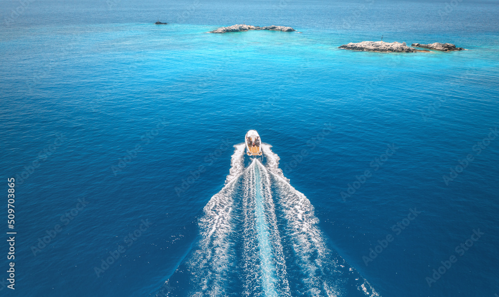 Aerial view of speed boat on blue sea at sunset in summer. Motorboat on sea bay, rocks in clear turq