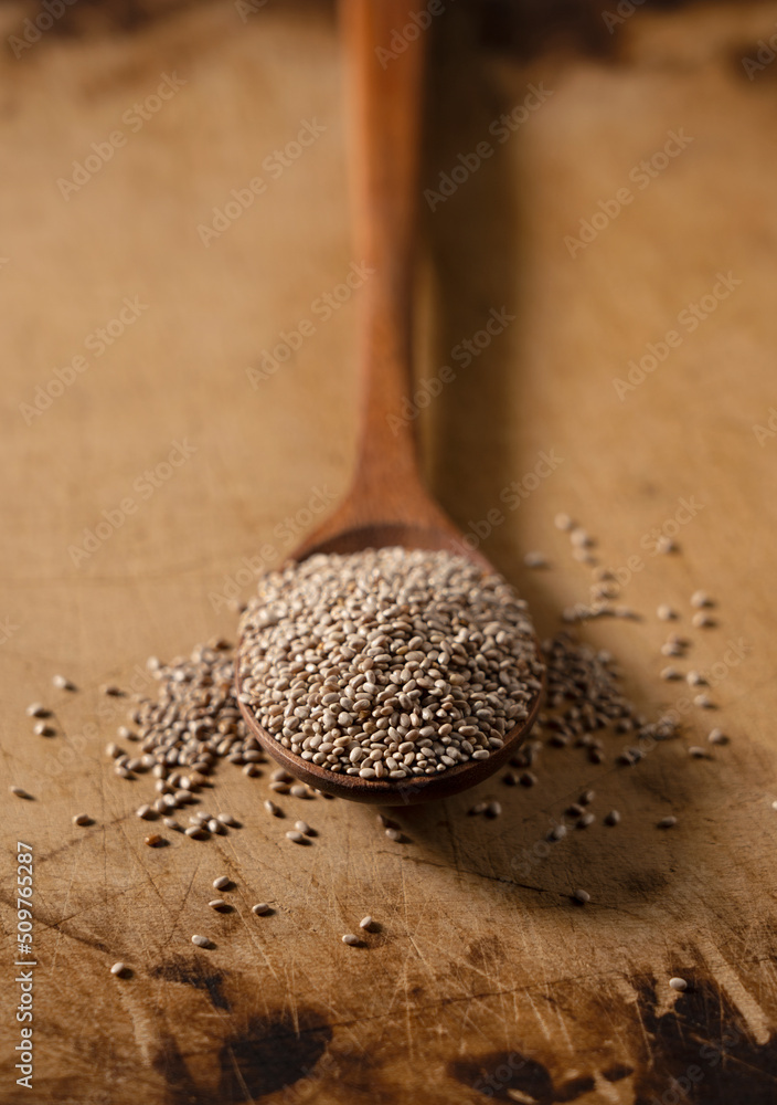 Wooden spoon and white chia seeds placed on wooden background.