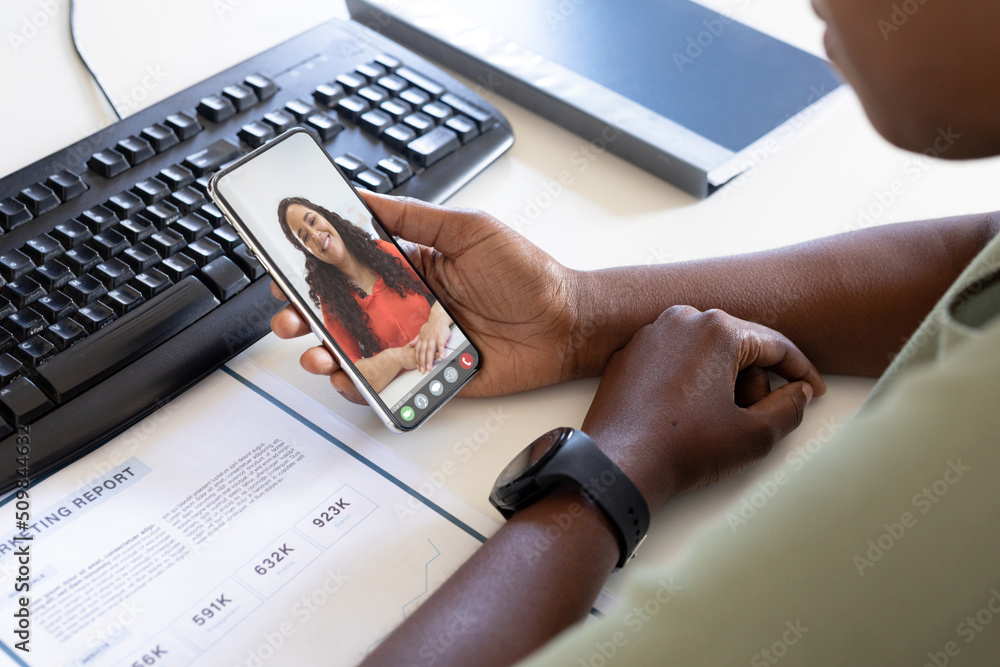 African american businessman video calling female coworker through smart phone in office