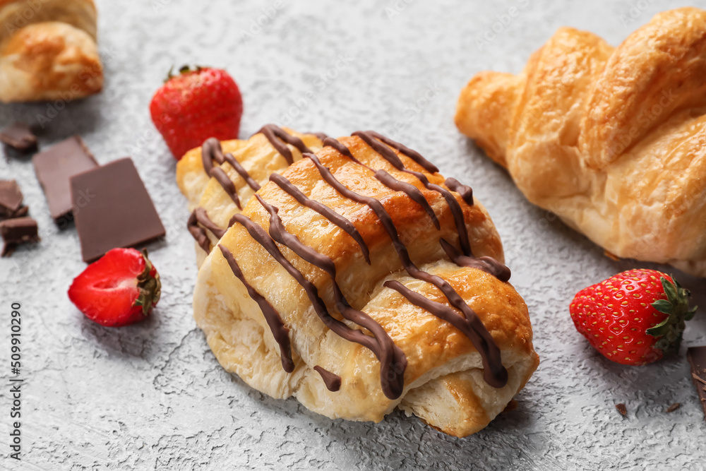 Delicious croissants with chocolate and strawberries on light background