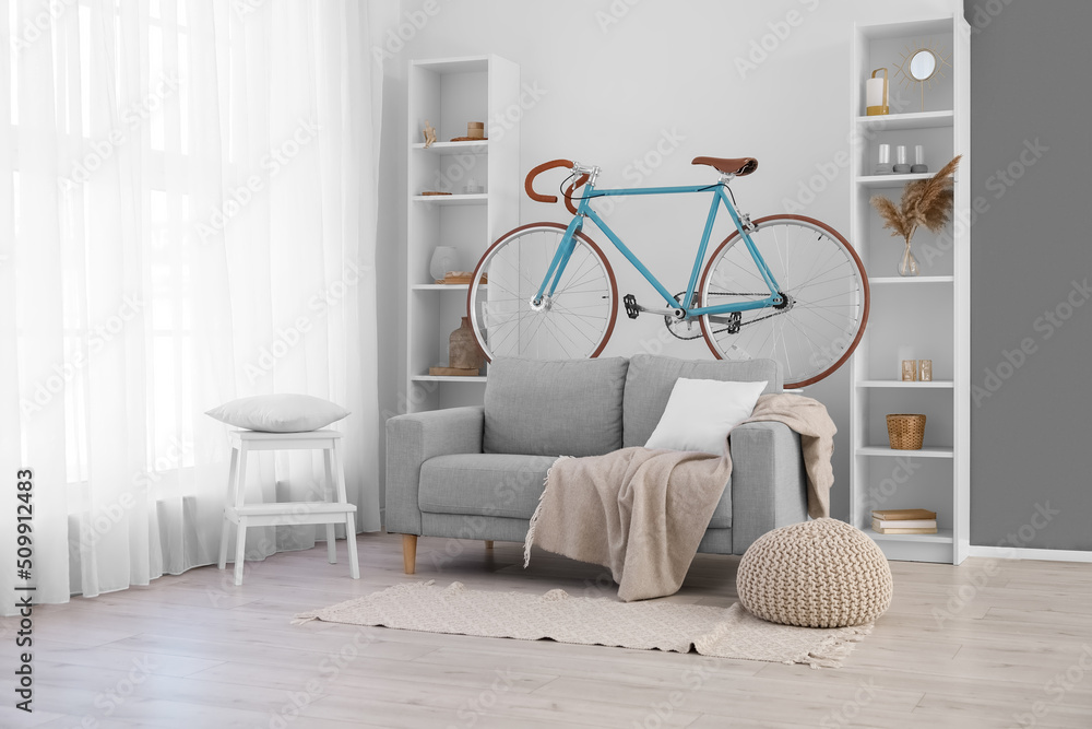 Interior of light living room with bicycle, grey sofa and shelving units